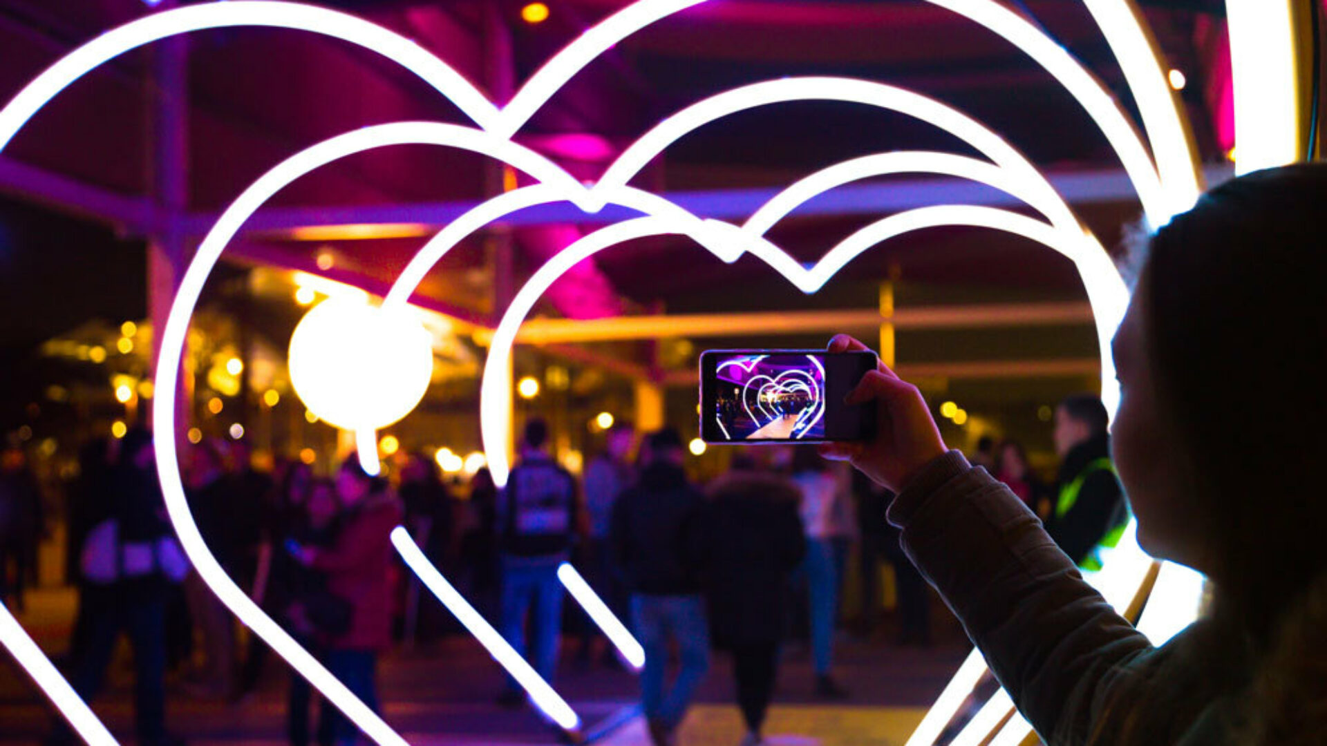 person holding phone in front of led heart tunnel