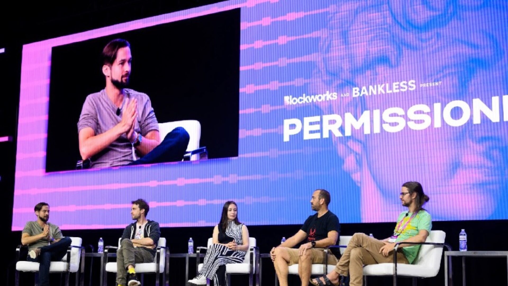 people sitting on chairs on stage at expo group's permissionless event