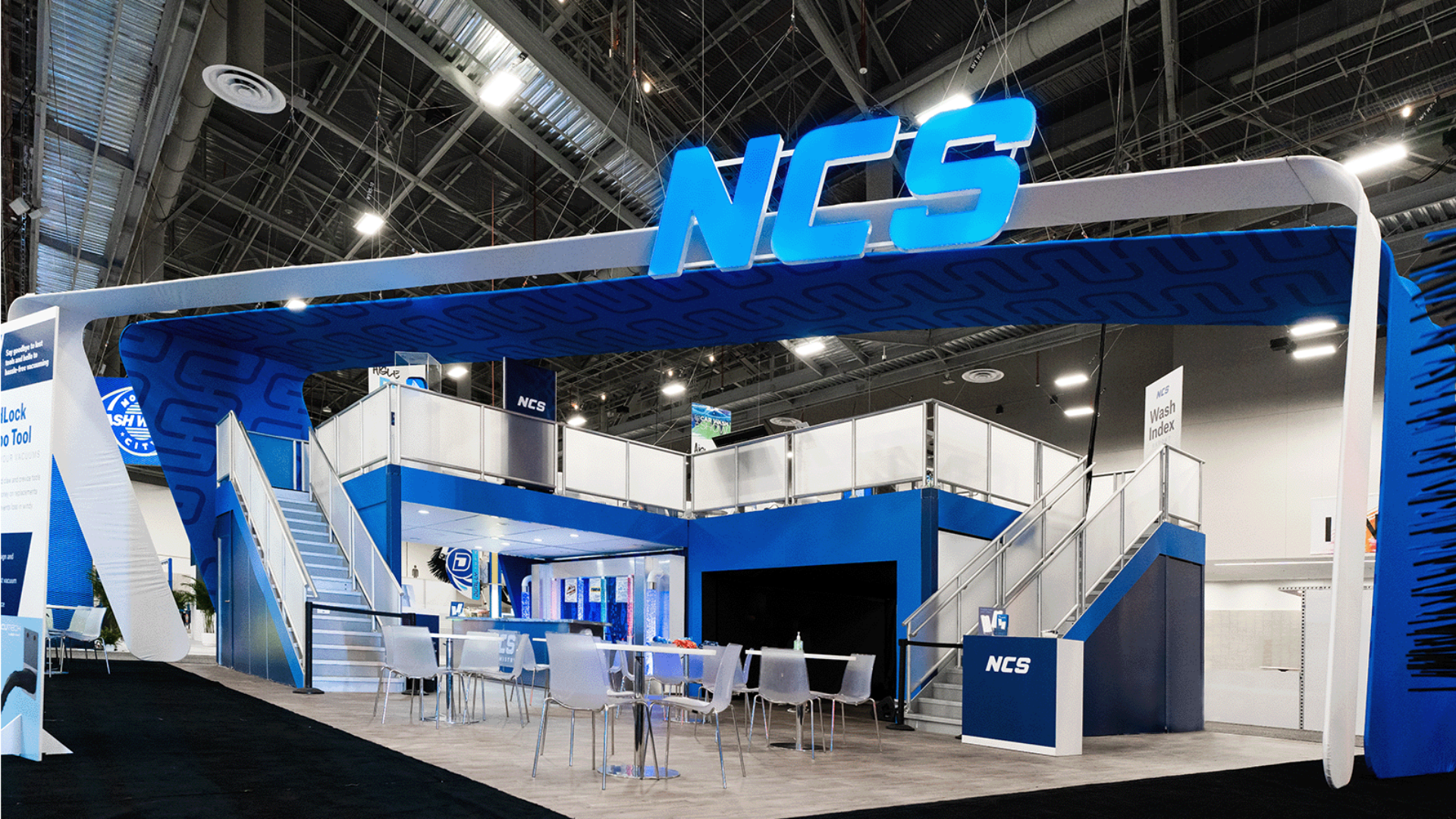 blue and white tradeshow booth with open floor plan, stair, and big NCS neon sign