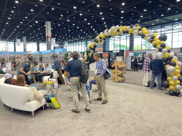people walking around a trade show with a yellow balloon arch in the background