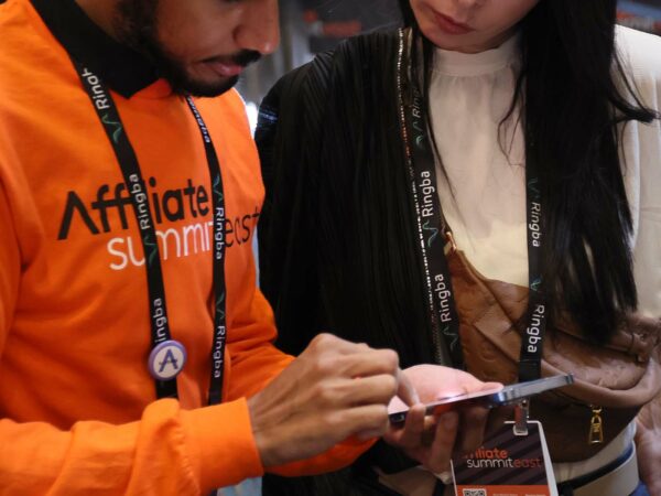 man in orange sweatshirt showing an ipad to a woman at trade show